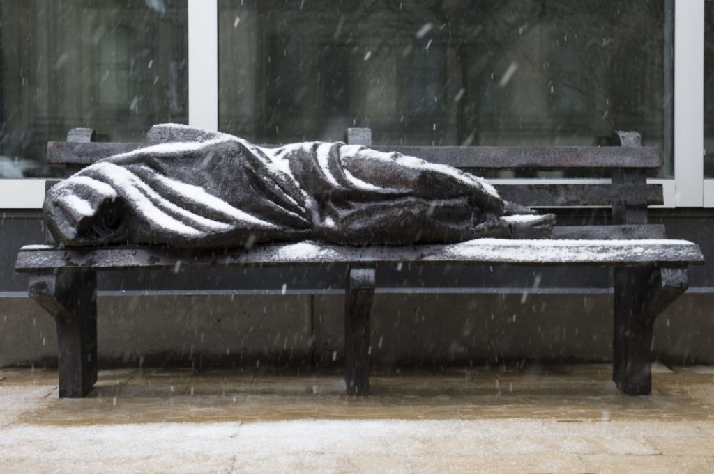 image of a homeless person sleeping on a bench while it snows